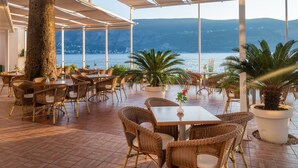Un espace extérieur aménagé pour les repas, avec des meubles en osier, des plantes en pot et une vue sur la mer et les collines.