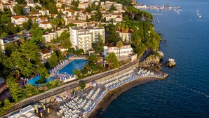 Vue aérienne d’un hôtel situé sur la côte, avec une piscine, des chaises longues sur la plage et une vue sur la mer et les montagnes.