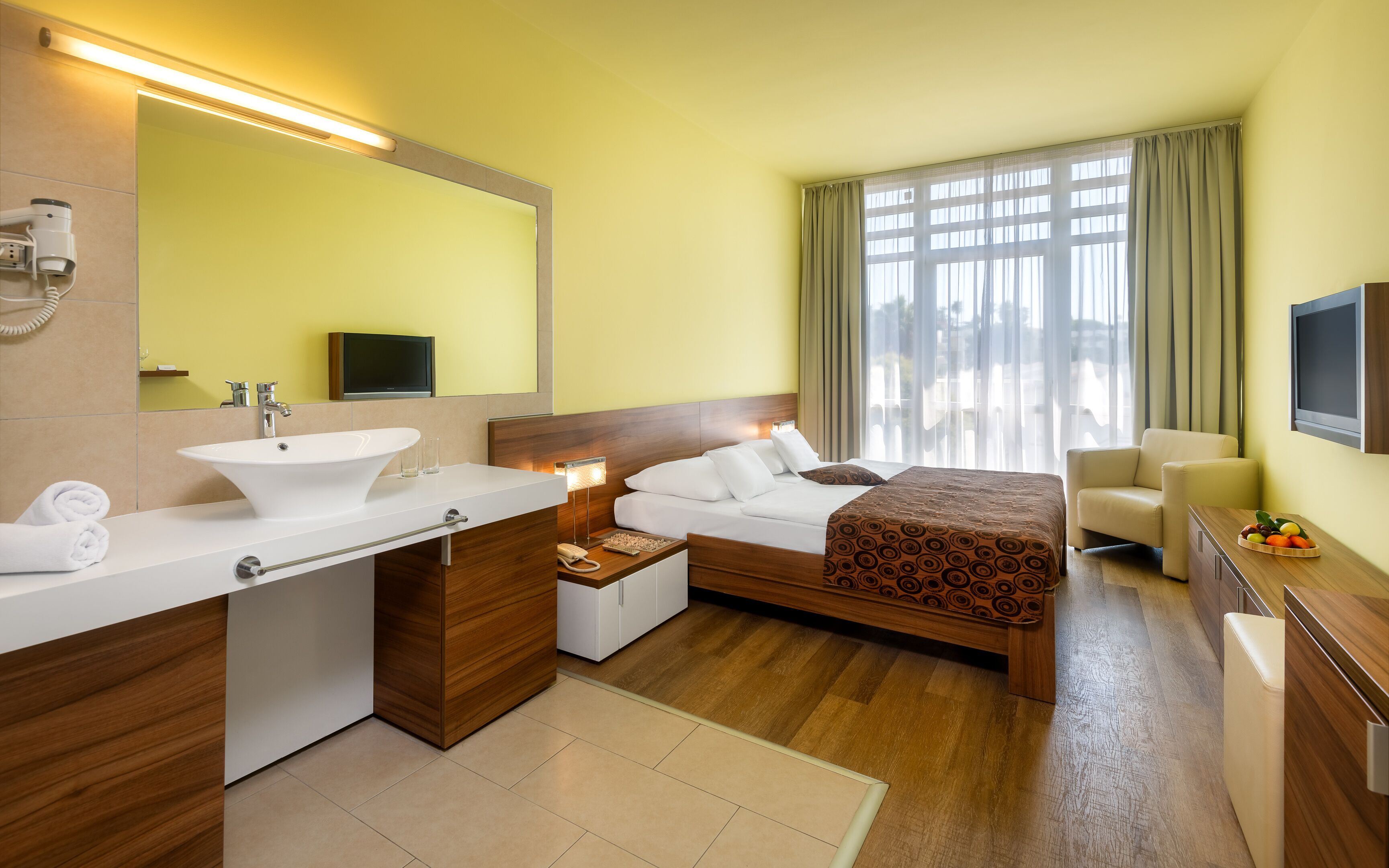 A hotel room with a large bed, a bedside table, a bathroom with a sink and mirror, and a television.