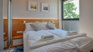 A neatly made bed with white linens and pillows, a wooden headboard, and two framed pictures on the wall. - Apartament z widokiem na morze - Nadmorski Luksus Apartamenty (Ustronie Morskie)