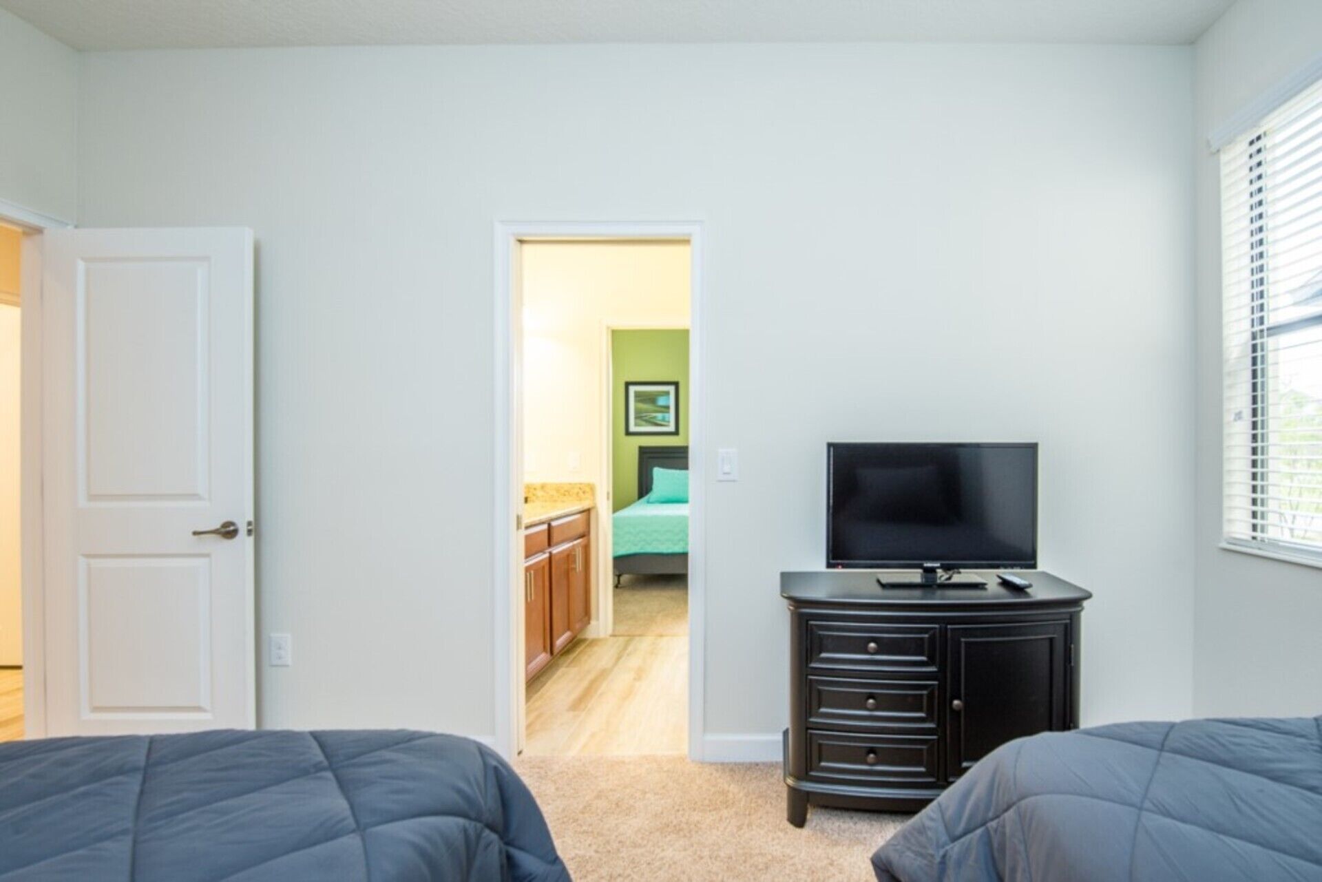 Un dormitorio con dos camas, un televisor sobre un tocador y una puerta que da a otra habitación.