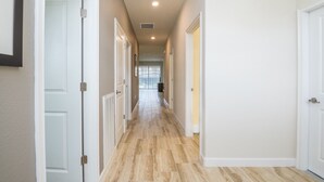 Un pasillo con puertas blancas, piso de baldosas e iluminación empotrada en el techo.