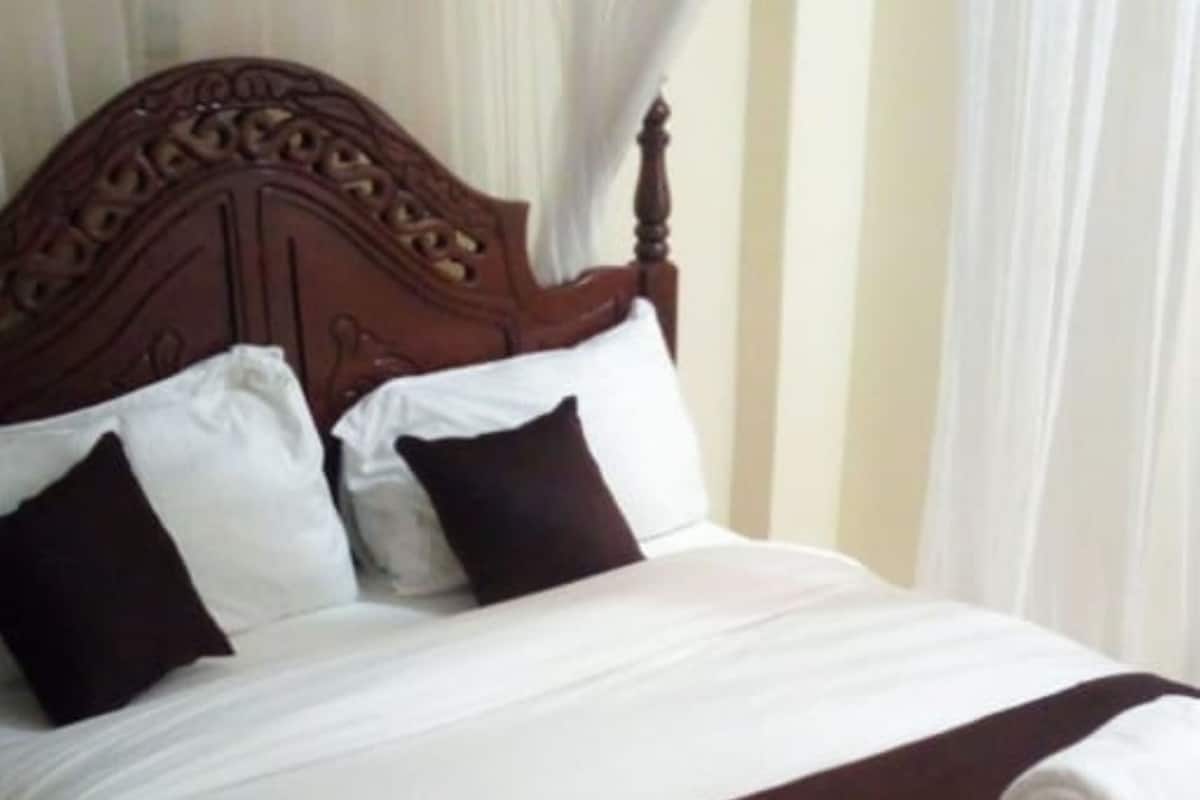 Una cama bien hecha con cabecera de madera, ropa de cama blanca y marrón, y una toalla enrollada al pie.