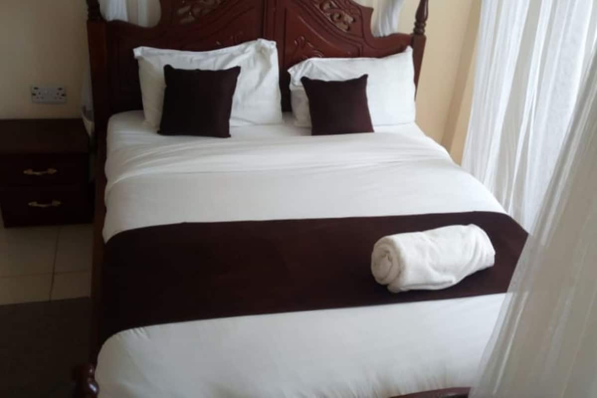 Una cama bien hecha con ropa de cama blanca y marrón, un cabecero de madera y una mesita de noche pequeña con cajones.
