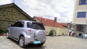 A silver SUV parked in a courtyard with a stone wall and a building with a red roof in the background. - MT Ararat Hotel (Nakuru)