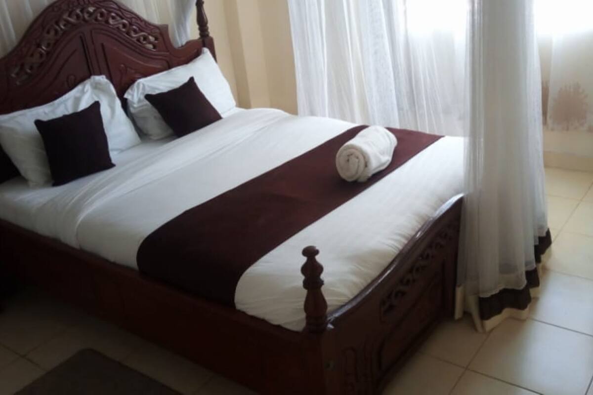 Una cama bien hecha con cabecera de madera, ropa de cama blanca y un detalle en tono café.