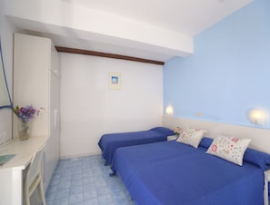 Een slaapkamer met twee bedden, een kaptafel, een vaas met bloemen en een foto aan de muur.