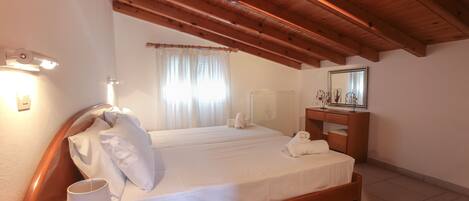 A bedroom with a wooden ceiling, a bed with white linens, a nightstand with a lamp, and a dresser with a mirror.