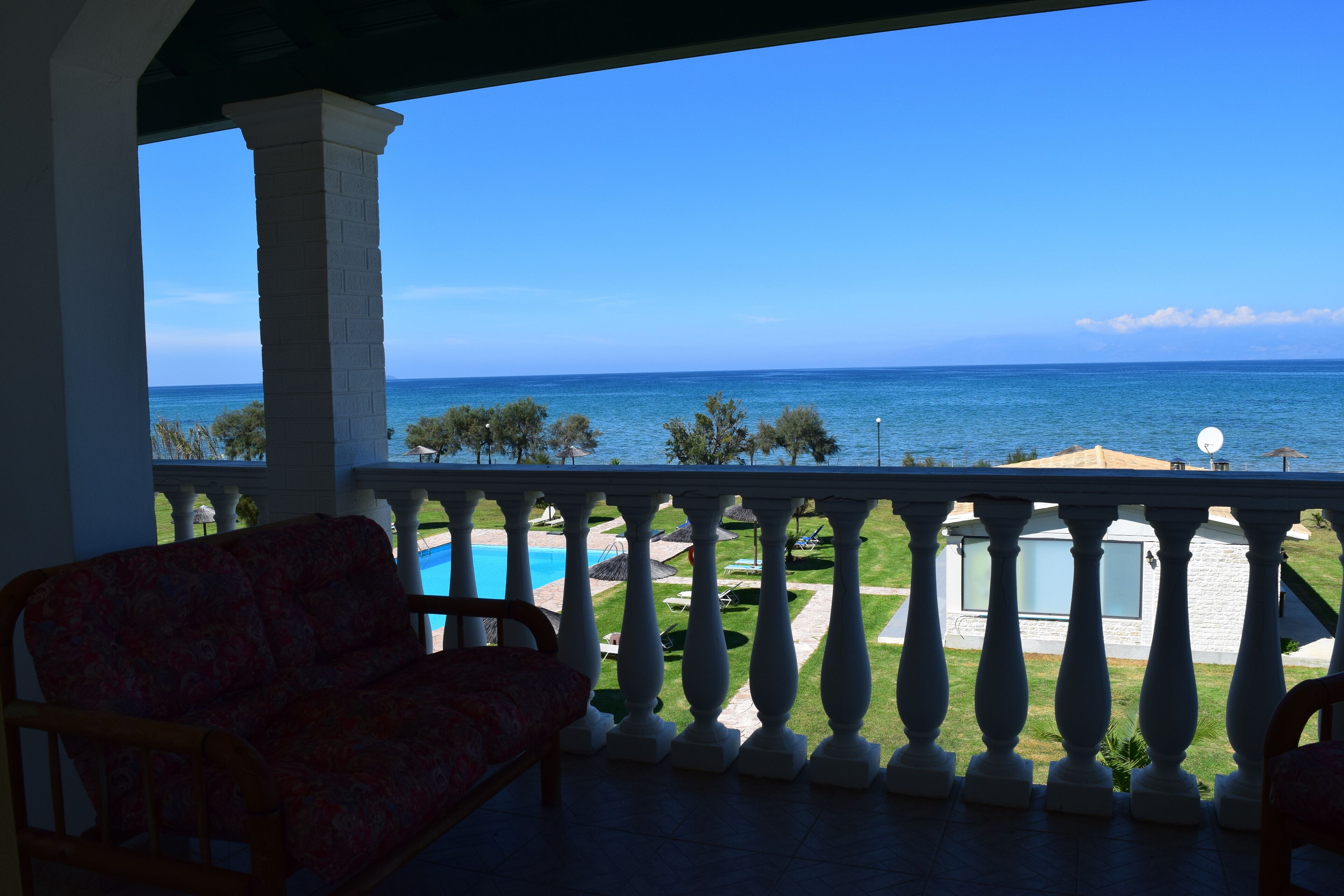 Un balcon avec vue sur la mer, une piscine et une pelouse agrémentée de parasols.
