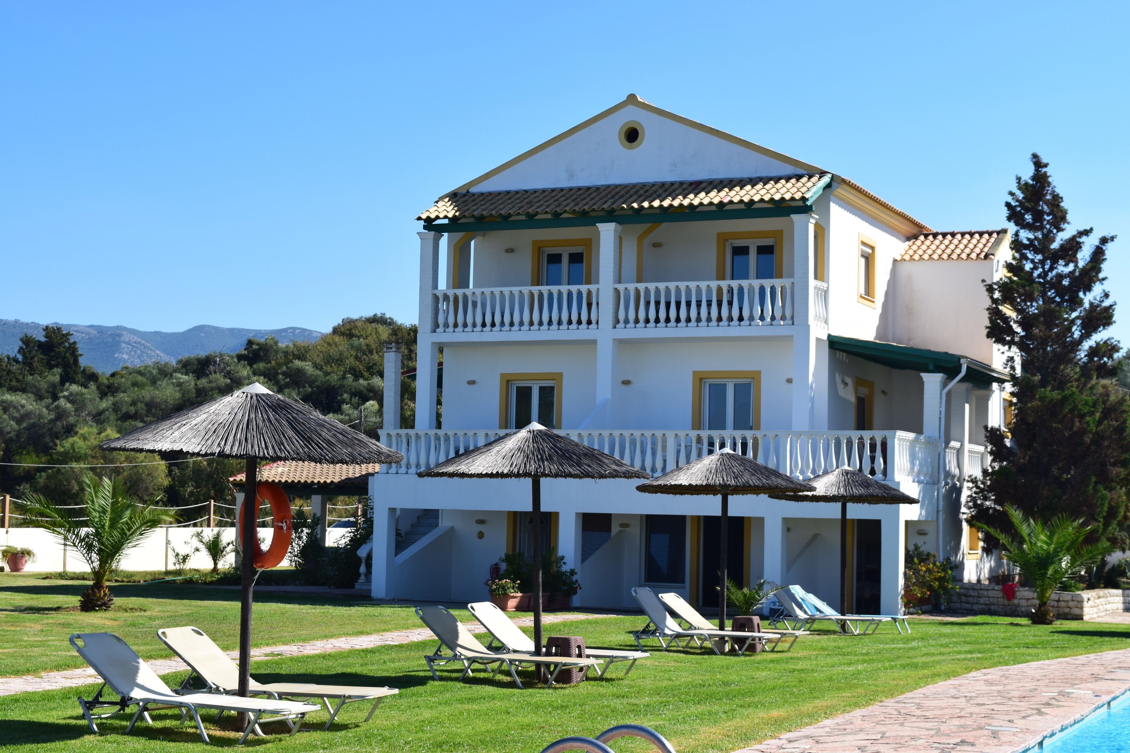 A two-story building with a balcony, a swimming pool, and lounge chairs.