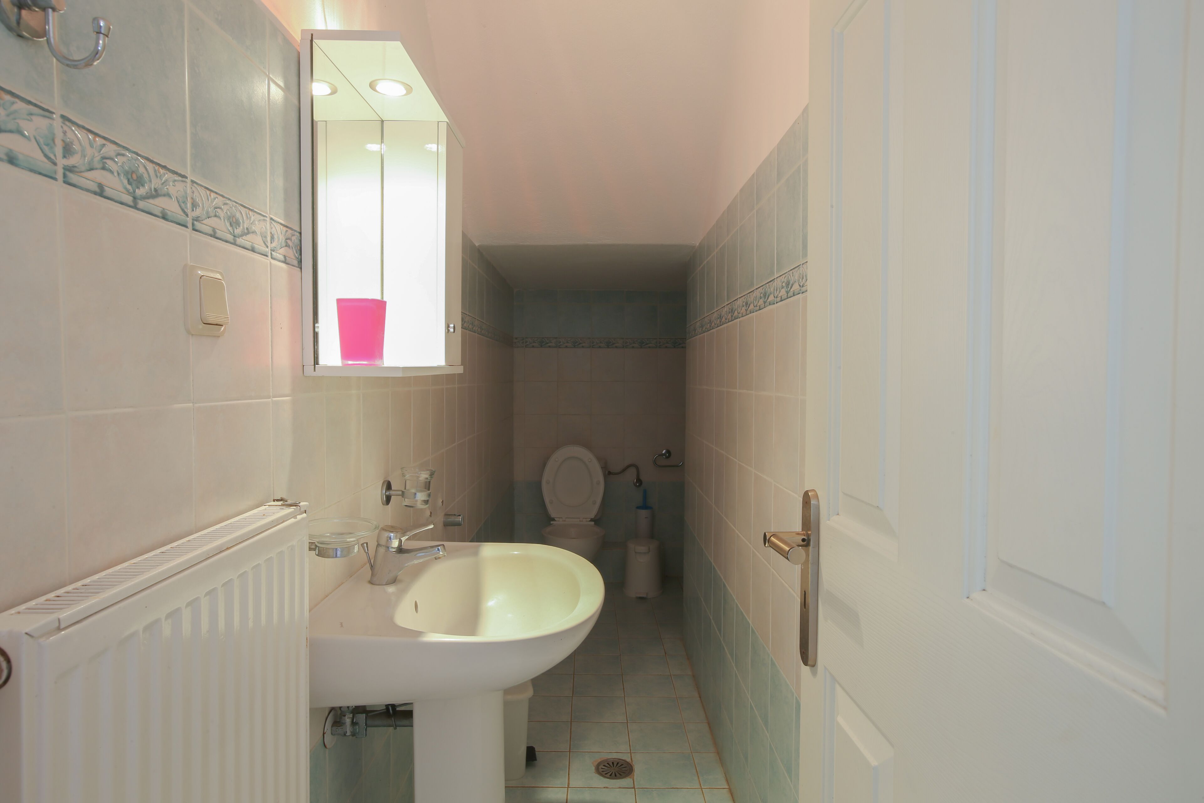 A narrow bathroom with a white sink, a mirror, and a toilet.