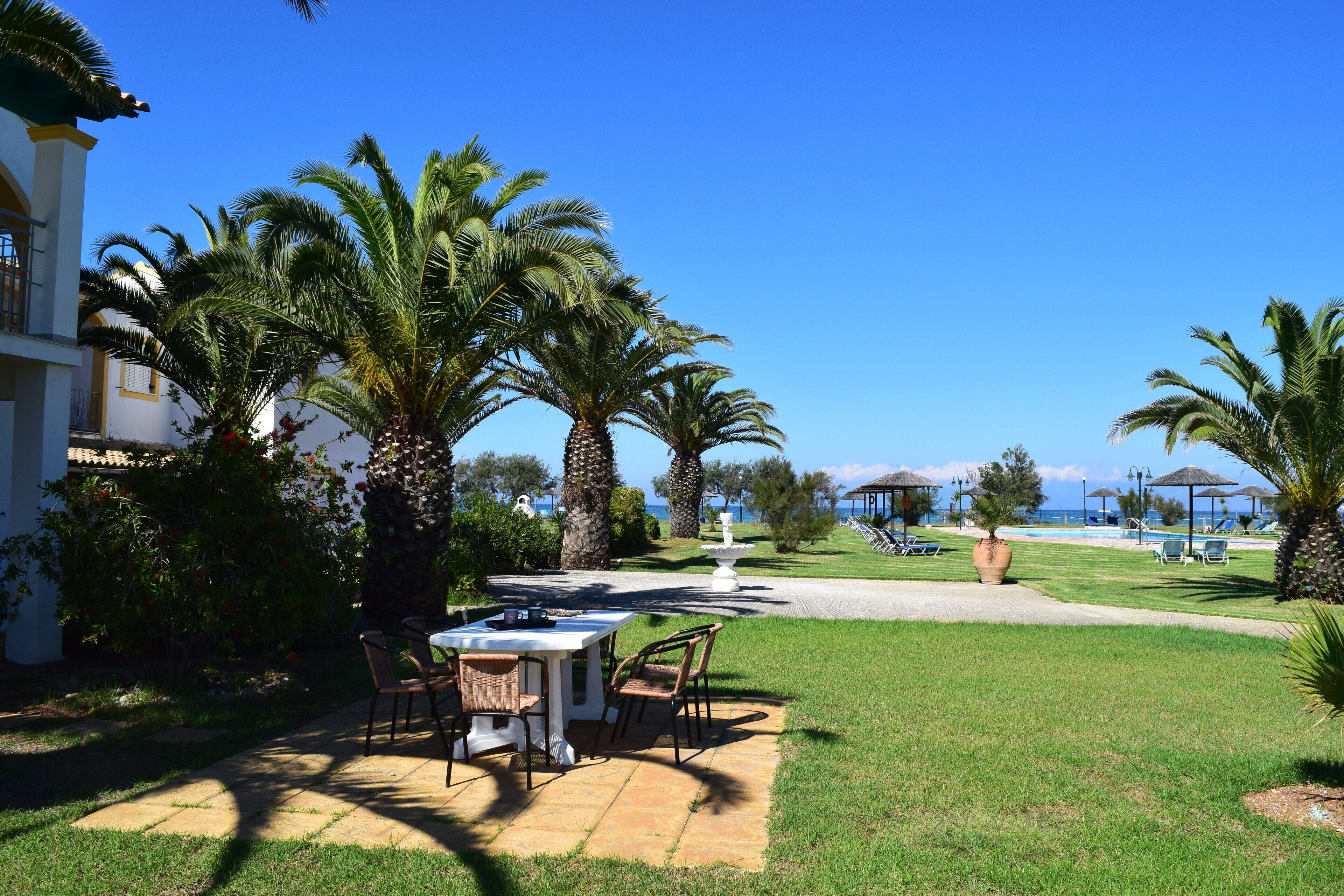 A patio with a table and chairs, surrounded by palm trees and a view of the sea.