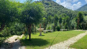 A paved pathway leading through a lush garden with a fountain and benches. - Room-michelangelo House, Bilo (Gioiosa Marea)