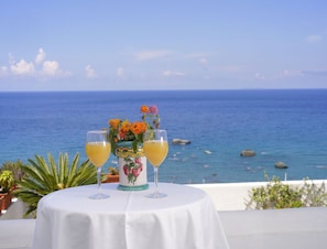 A table with two glasses of orange juice and a floral vase, set against a backdrop of the sea and sky. - Room in B&B - Ischia, 1 Relaxing Doubles Hotel Imperamare (Forio)