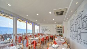 A restaurant with tables set for dining, a view of the sea, and a wall with a cityscape mural. - Room in B&B - Ischia, 1 Relaxing Doubles Hotel Imperamare (Forio)