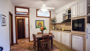 Eine Küche mit weißen Schränken, einer Mikrowelle, einem Backofen und einem Geschirrspüler. Es gibt einen Esstisch mit Stühlen und einen Deckenventilator.