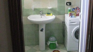 A small bathroom with a sink, mirror, green tiles, a washing machine, and a Mickey Mouse rug. - Zaleuco Apartment - Ideal for Families (Locri)