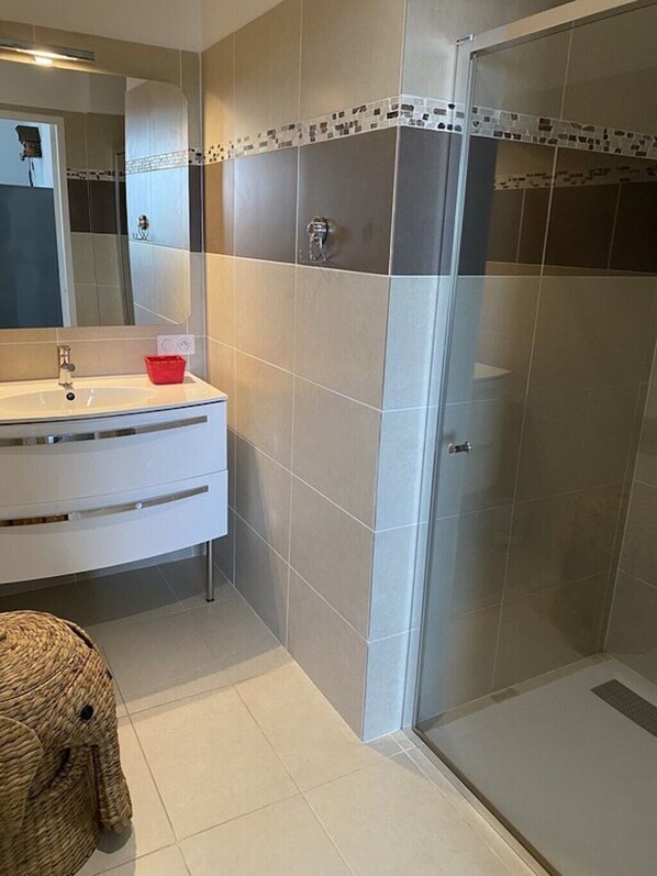 Ein modernes Badezimmer mit einem weißen Waschtisch, einer Glasdusche und einem großen Spiegel.