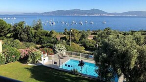 Une piscine avec vue sur la mer et les bateaux, entourée de verdure et de maisons.