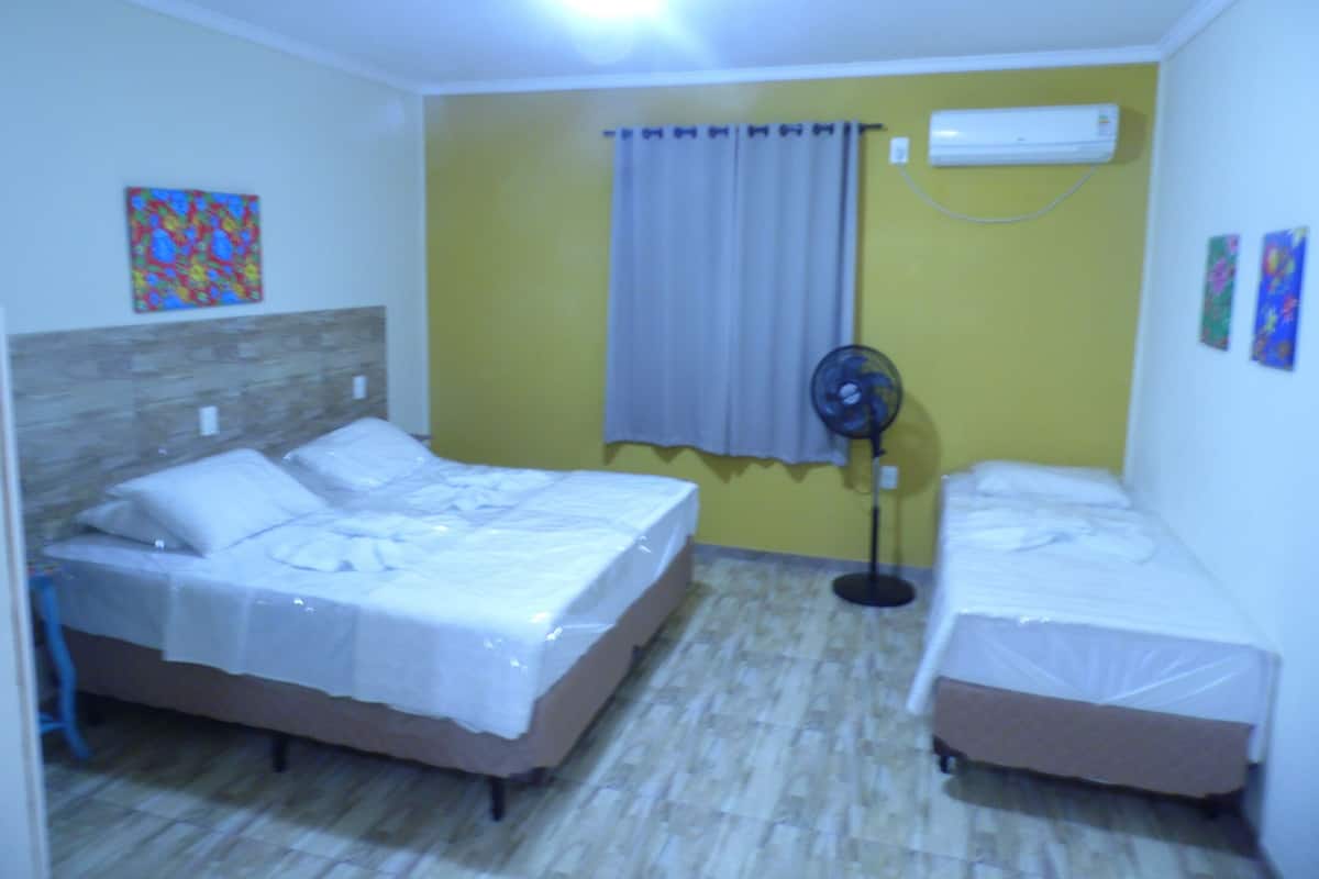 A room with two beds, a ceiling fan, an air conditioner, and a window with curtains.