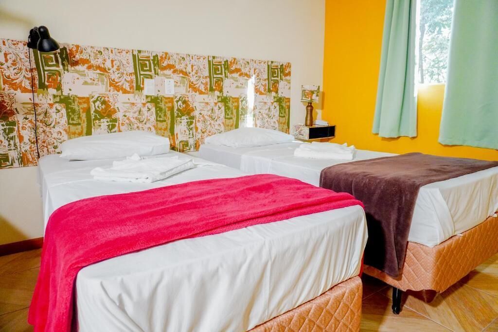 Een hotelkamer met twee bedden, een bekledingspaneel met een patroon, een nachtkastje en een raam met gordijnen.