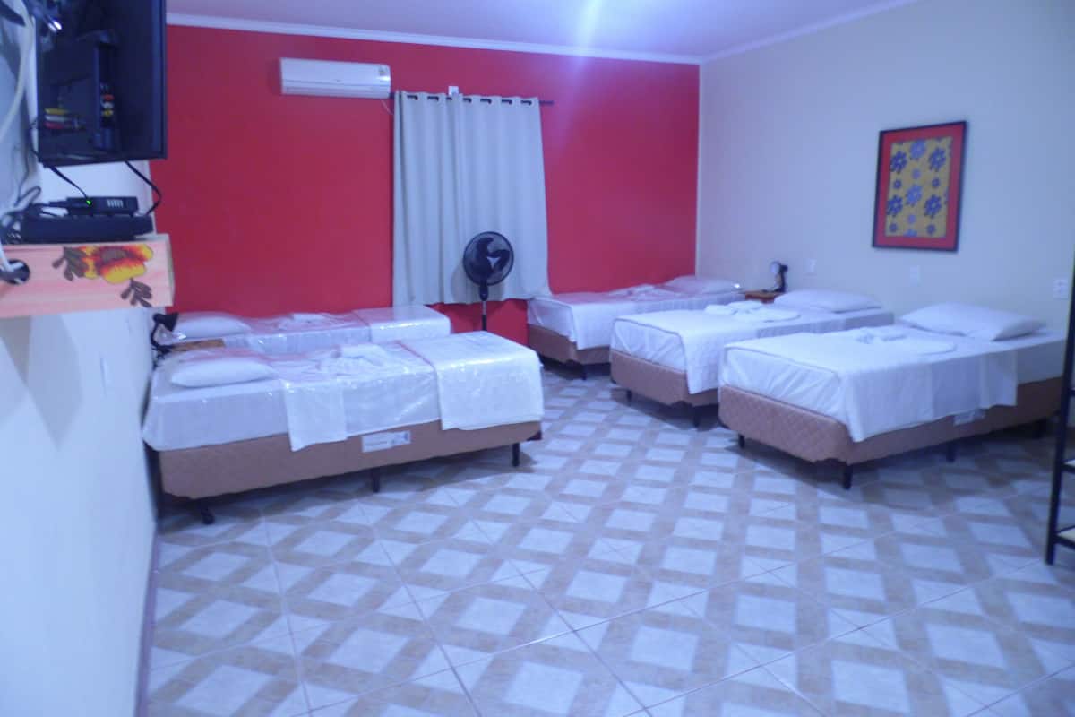 A hotel room with four beds, a fan, an air conditioner, and a tiled floor.