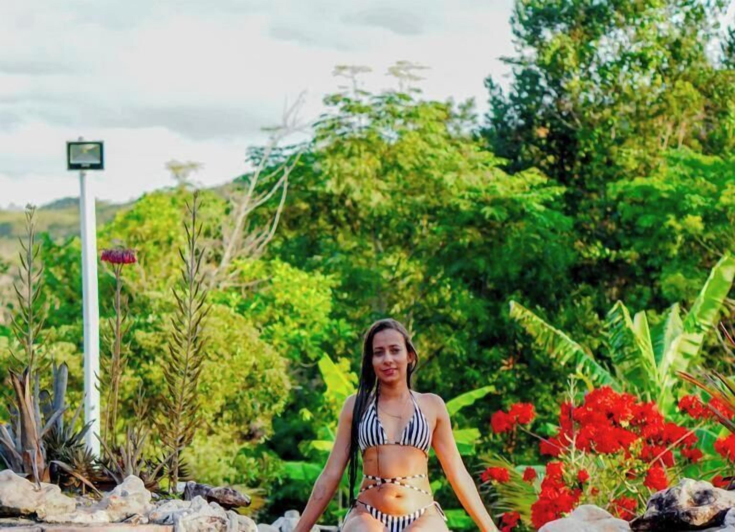 A person standing in a natural setting with greenery and rocks.