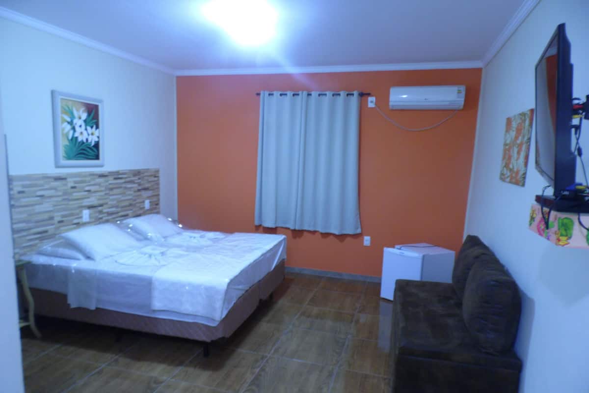 A bedroom with a bed, a nightstand, a dresser, a window with curtains, and a wall-mounted air conditioner.