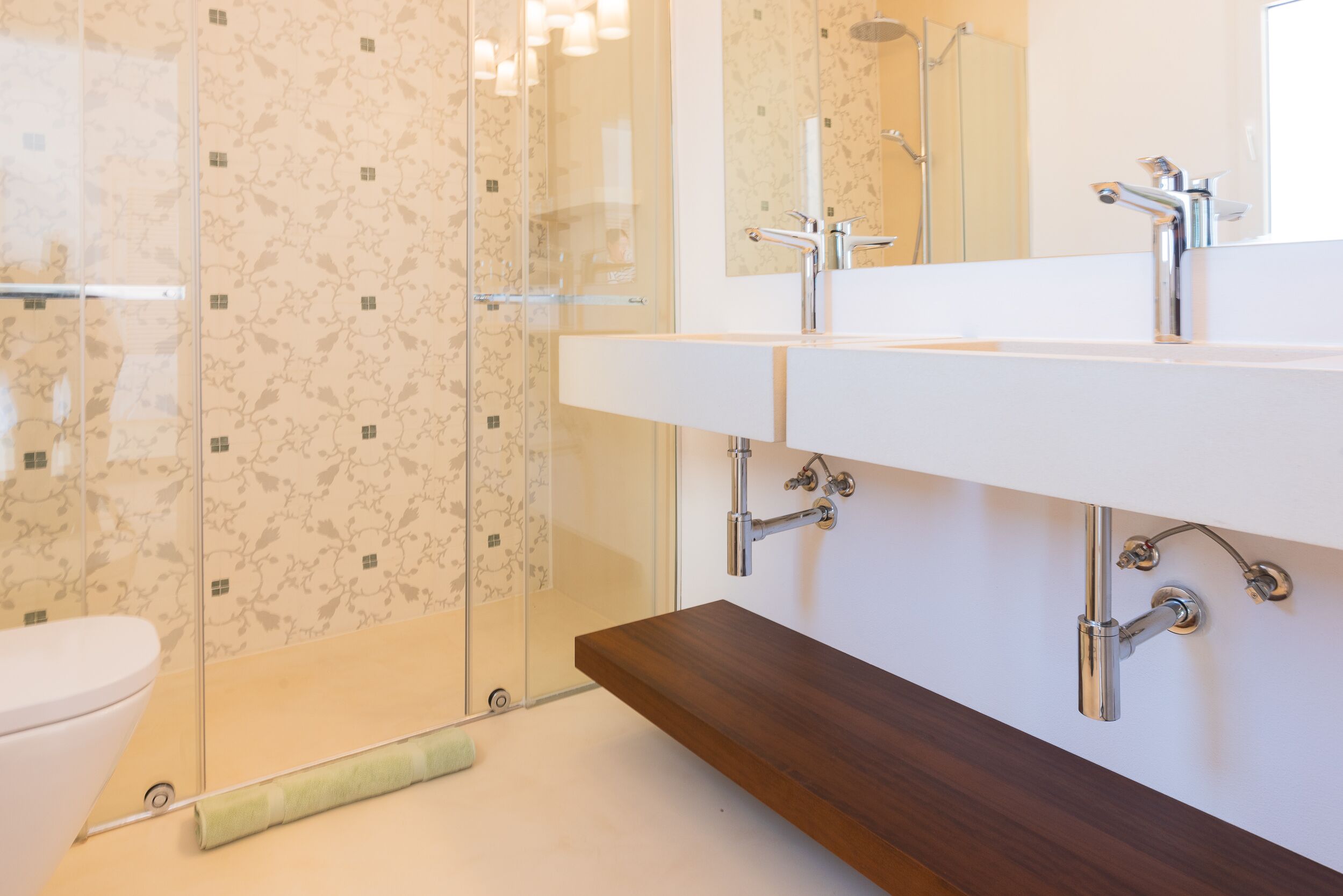 Een moderne badkamer met een douchecabine van glas, een witte wastafel met een houten aanrechtblad, en een spiegel boven de wastafel.