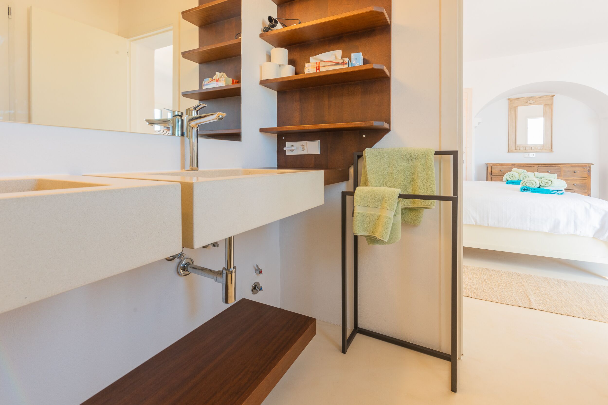 A modern bathroom with a large mirror, wooden shelves, a sink, and a towel rack.