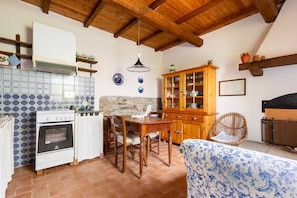 A kitchen with a stove, dining table, and chairs, a wooden cabinet, and a hanging light fixture.