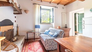 Ein gemütliches Zimmer mit Holzbalkendecke, einem fenster mit Vorhängen, einem gemusterten Sofa, einem Holztisch und einer Heizung.