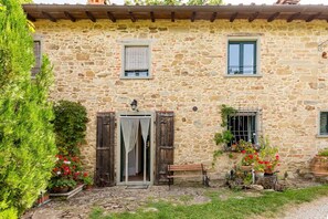 A stone building with a rustic entrance, a bench outside, and potted plants.