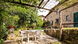 Ein Steinhhaus mit Garten-Terrasse, einem Tisch mit Stühlen und einem hölzernen Spalier.