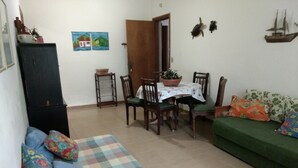 Ein Wohnzimmer mit Schachbrettmuster-Teppich, einem grünen Sofa, einem Esstisch mit Stühlen und einem Schrank.