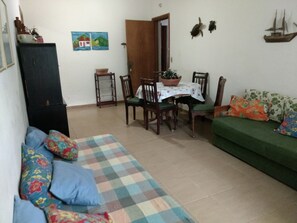 Uma sala de estar com tapete xadrez, sofá verde, mesa de jantar com cadeiras e um armário.