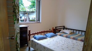 Ein Schlafzimmer mit zwei Betten, einem Holzschrank, einem Fenster mit Blick ins Grüne und einem gefliesten Boden.