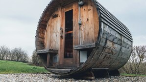 A cylindrical wooden structure with a door and a small window, situated on a gravel surface.