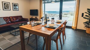 A dining area with a wooden table set for four, a leather sofa, and a TV on the wall.