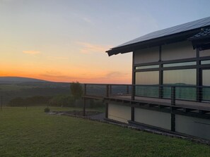Een modern gebouw met grote ramen en een balkon met uitzicht op een grasveld.