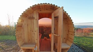 A wooden sauna with a circular design, featuring a bench and a small table inside.