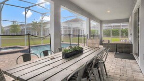 Un patio couvert avec une piscine, des sièges d’extérieur et une table en bois.