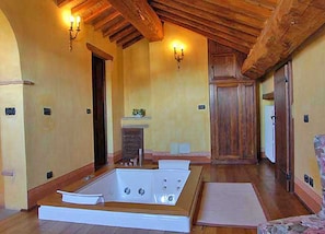 A spacious room with a large bathtub, wooden ceiling beams, and a fireplace.