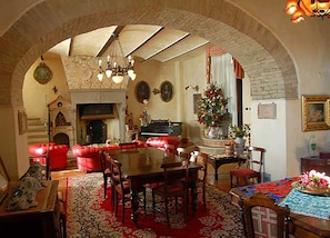 A cozy living room with a fireplace, red leather sofa, wooden dining table, and a Christmas tree.