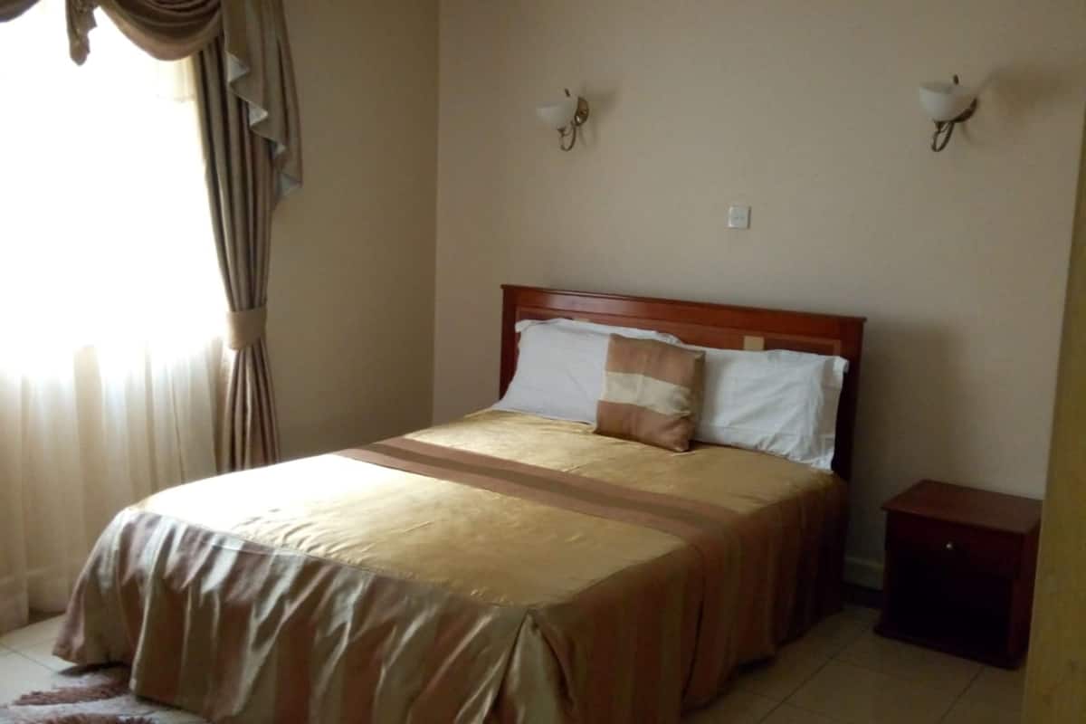 A bedroom with a bed, curtains, a nightstand, and a wall-mounted light fixture.