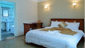 Habitación de hotel con cama, mesita de noche, lámpara y baño visible a través de una puerta abierta.
