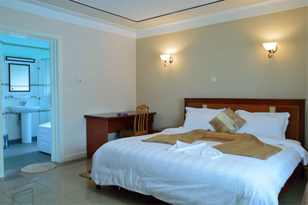 A hotel room with a bed, bedside table, lamp, and a bathroom visible through an open door.