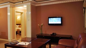 Habitación de hotel con sofá de cuero marrón, una mesa de centro de madera, un televisor de pantalla plana montado en la pared y un escritorio con un florero.