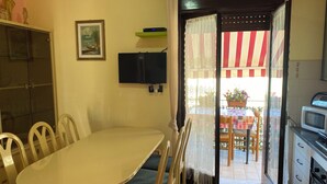 A dining area with a table and chairs, a television, and a kitchen with a microwave. - Apartment Direct to the Beach of Scala Dei Turchi (Realmonte)