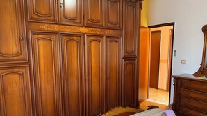 A bedroom with a large wooden wardrobe, a bed with a striped bedspread, and a wooden dresser with a mirror. - Apartment Direct to the Beach of Scala Dei Turchi (Realmonte)